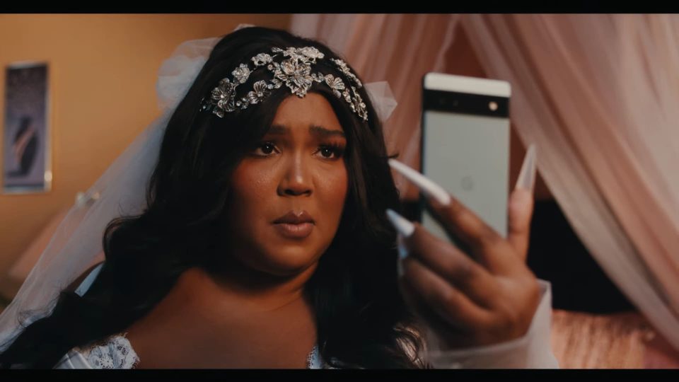 Lizzo in a bridal gown holding a Pixel 6a