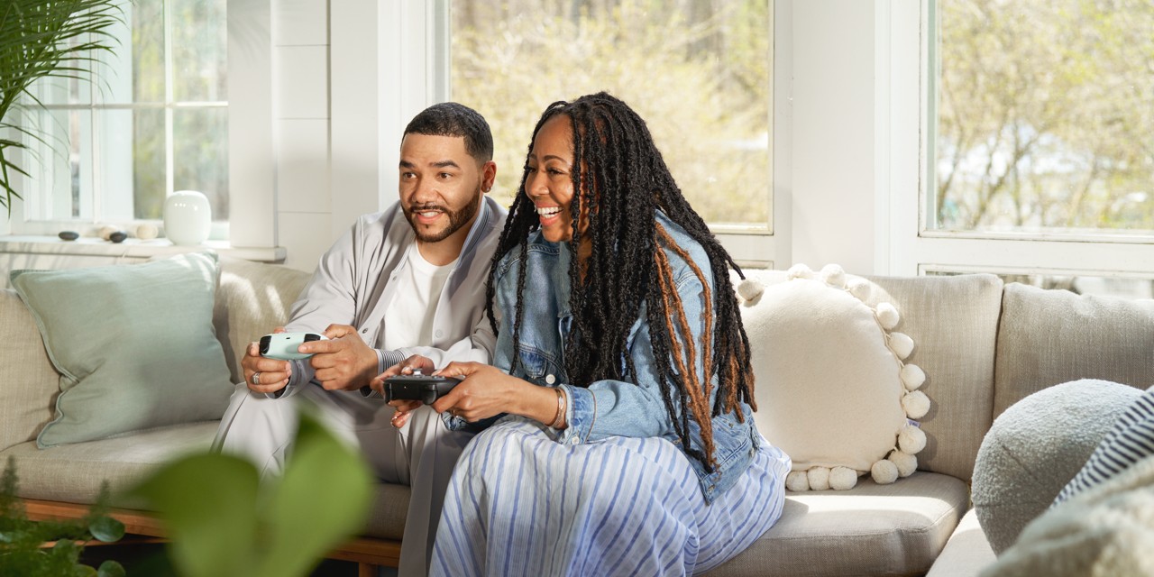 Two people holding Stadia Controllers with a Nest Wifi Pro in the background