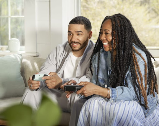 Two people holding Stadia Controllers with a Nest Wifi Pro in the background